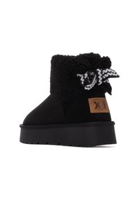 Botines de ante negros con un acolchado negro esponjoso en el cuello, un lazo decorativo con un patrón en negro y plateado, y una etiqueta de logo de cuero marrón.