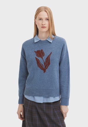 Light blue knitted sweater with a burgundy tulip design at the center. Features a ribbed hem and dropped shoulders, layered over a blue collared shirt.
