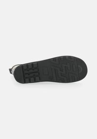 Black rubber shoe sole featuring a textured pattern with various rectangular and zigzag tread designs. Smooth edges with a rounded toe.