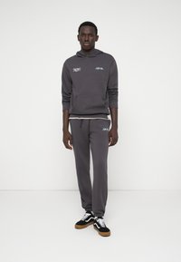 Sweatshirt cinza e calças de fato correspondentes feitas de um tecido de algodão misto com um ajuste relaxado. Apresenta bolso, punhos e acentos de logotipo contrastantes.