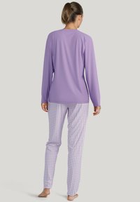 Paarse lange mouwen top gecombineerd met lichtpaarse pyjamabroek in een ruitpatroon. De stof lijkt zacht en lichtgewicht. Eenvoudige, relaxte pasvorm.