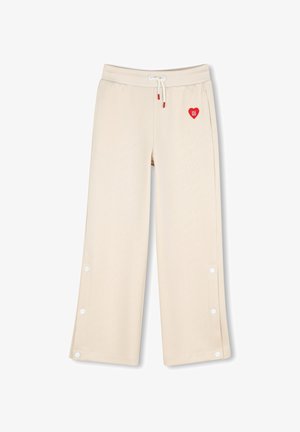 Beige wijde broek met trekkoord in de taille, zijdrukknopen langs de pijpen en een klein rood hartlogo vlak bij de zak.