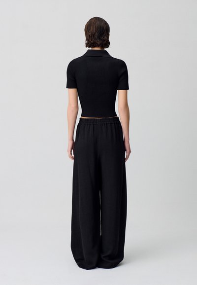 Top corto a righe nere con maniche corte abbinato a pantaloni neri larghi. Design semplice, vita elastica, tessuto morbido, styling minimale.