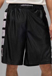 Shorts de sport noirs en tissu brillant, avec des panneaux latéraux blancs, des détails en rayures et le numéro "23" en gras sur la jambe gauche.