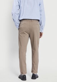Beige chino's met een recht model, voorzien van twee achterzakken, riemlussen en opgerolde cuffs, gecombineerd met een blauw gestreept shirt.