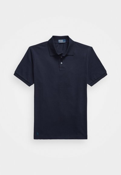 Tums zila polo krekls no teksturēta auduma, ar divu pogu apkakli un mazu izšūtu logotipu apakšmalā. Īsas piedurknes.