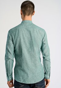 Lange mouwen shirt van textuur lichtgroene stof. Heeft een button-down kraag, knoopmanchetten en een rechte zoom.