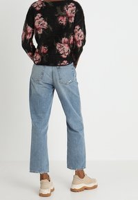 Maglione nero lavorato a maglia con motivo floreale rosa, abbinato a jeans azzurri a gamba dritta e scarpe da ginnastica beige con dettagli crema.