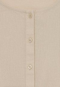 Bēša lina blūze ar apaļu kakla izgriezumu un piecām pogām priekšpusē, ar teksturētu auduma apdari.