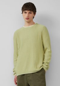 Hellgrüner gerippter Pullover mit langen Ärmeln und rundem Halsausschnitt, der eine feine Textur und eine lockere Passform aufweist, kombiniert mit olivfarbenen Hosen.