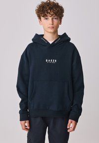 Marineblå hættetrøje lavet af blødt stof, med en kængurulomme og hvidt "BAKER"-logo på brystet. Inkluderer snore ved huen.