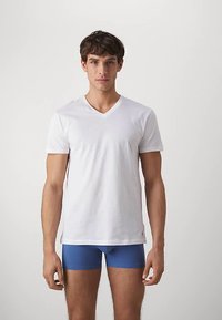 White cotton V-neck t-shirt with short sleeves, worn over blue boxer briefs. Smooth texture and fitted design, with subtle brand logo detail.