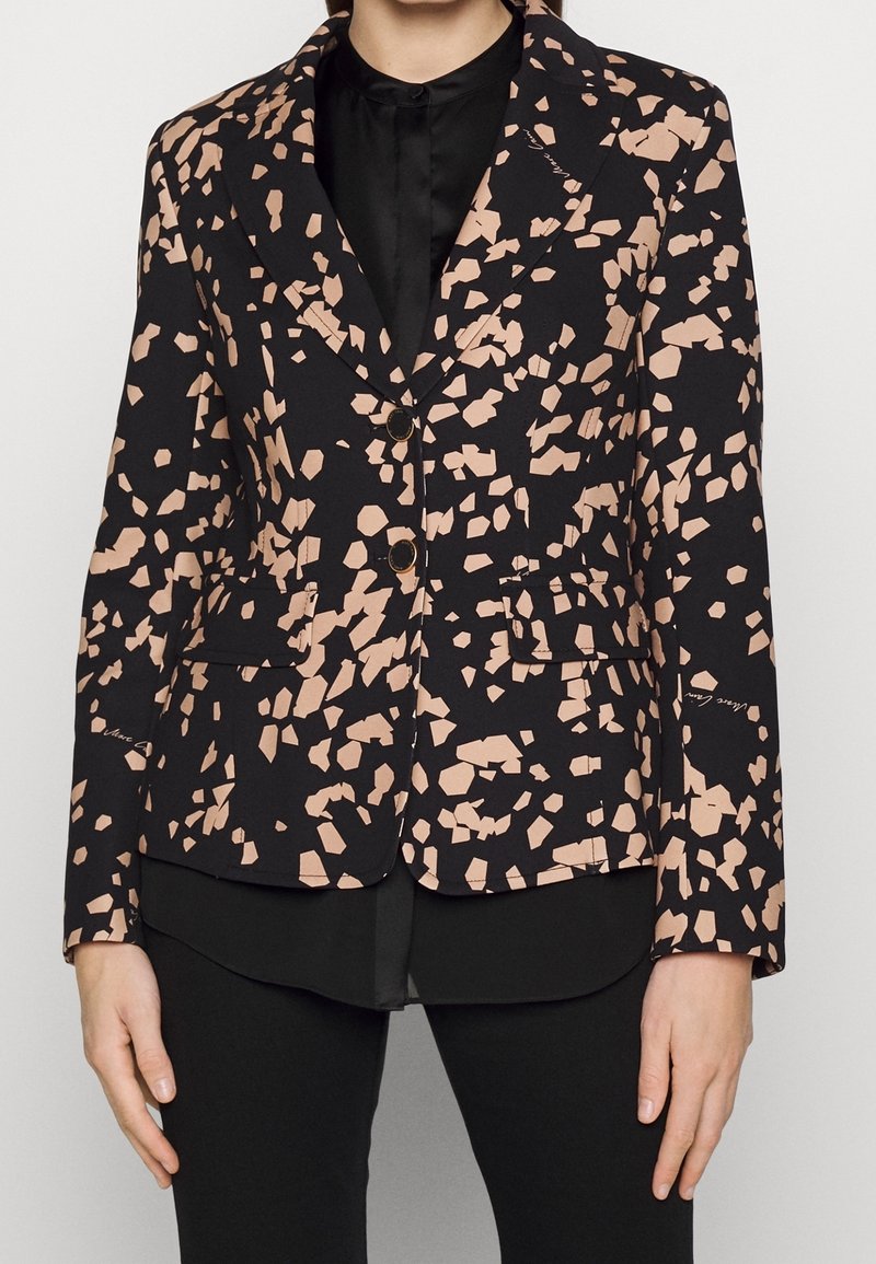 Blazer avec un fond noir et un motif nu abstrait, présentant un col cranté, deux poches avant et deux boutons à l'avant.