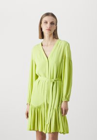 Lime green button-up dress with a v-neck, long sleeves, elastic cuffs, a waist tie, and a flared ruffled hem. Smooth fabric texture.