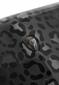 Schwarzer Hartschalenkoffer mit glänzender Oberfläche und mattem dunklen Muster. Verfügt über ein metallisches Heys-Logo-Emblem.