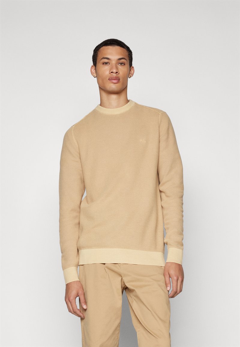 Beige gestrickter Pullover mit Rundhalsausschnitt, gerippten Bündchen und Saum. Besitzt ein subtil strukturiertes Muster und ein kleines Logo auf der Brust.