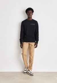 Felpa navy con logo "GANT 1949", pantaloni beige e sneakers bianco e nero. Design semplice, tessuto morbido, vestibilità rilassata.