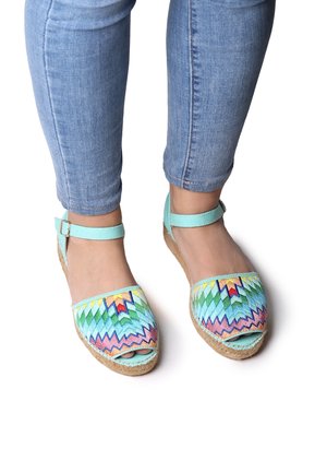 Pies con alpargatas de punta abierta con patrón de zigzag colorido y tiras en el tobillo, combinadas con vaqueros pitillo azul claro.