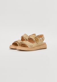 Zlatne sandale s pletenicama i podesivim trakama, platforma u stilu espadrila i teksturirani detalji na trakama. Glatka smeđa unutrašnjost.