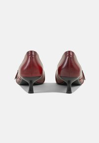Zapatos de tacón alto de cuero rojo con punta afilada y un tacón pequeño, que presentan un diseño minimalista y una textura suave.