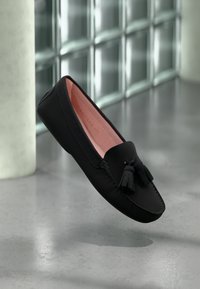 Čierne kožené loafers s ružovým interiérom, so zaoblenou špičkou a ozdobami v podobe strapcov, vystavené na minimalistickom pozadí.