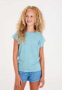 Camiseta de manga corta azul claro con cuello redondo y un bordado de "Buena Suerte" en el pecho, combinada con pantalones cortos de mezclilla.