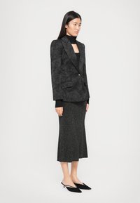 Black patterned blazer with a single button, paired with a fitted black ribbed top and a sparkly black midi skirt, finished with black mules.