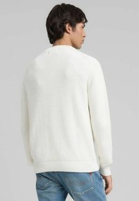 Maglione bianco a maglia con texture a coste, scollo rotondo e spalle scese, abbinato a jeans di denim blu, mostrato da dietro.