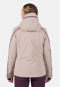 Beige waterdichte jas met een getailleerd ontwerp, hoge kraag en verstelbare capuchon. Heeft donkerpaarse accenten langs de mouwen. Gladde textuur.