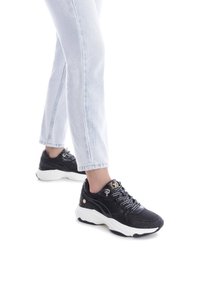 Zapatillas atléticas negras con suelas blancas, acentos texturizados y detalles en dorado en los cordones. Combinadas con unos vaqueros rectos de lavado claro.