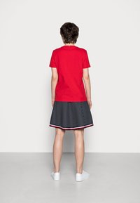 Röd t-shirt med kort ärm, kombinerad med en svart-vitrandig kjol med röd kant, och vita sneakers.