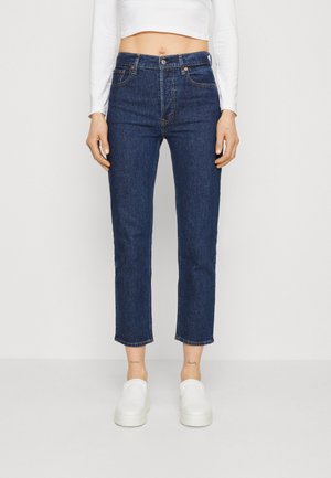 Jeans τζην σε σκούρο μπλε, με ψηλή μέση, cropped μήκος ως τον αστράγαλο, πέντε τσέπες και κουμπωτό φερμουάρ. Σε συνδυασμό με λευκά slip-on παπούτσια.