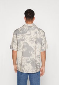 Camisa de manga corta hecha de tela tejida, con un patrón abstracto en beige y gris, con un corte relajado y cuello puntiagudo.
