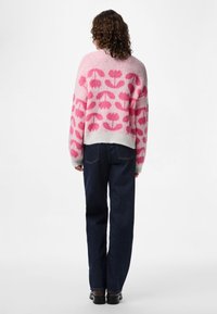 Pink and white sweater with floral pattern, made of soft material, featuring a cropped design and long sleeves, paired with dark denim jeans.