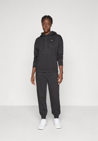 Schwarzer Hoodie mit Kordelzug, Kängurutasche und Logo. Kombiniert mit schwarzen Sweatpants. Weiße Sneaker runden das lässige Outfit ab.