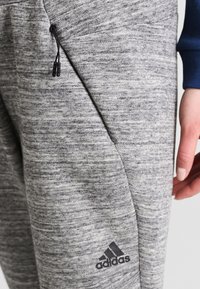 Grå texturerade joggers med dragsko i midjan, sidfickor och en svart Adidas-logotyp på underbenet.