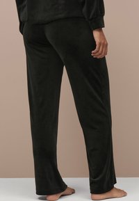 Sorte velour pyjamasbukser med et lige ben-design og elastisk talje, der har en glat tekstur uden synlige mønstre eller detaljer.