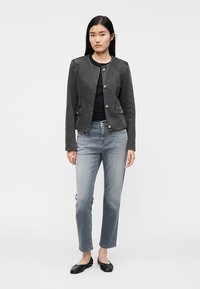 Giacca di denim grigia con scollo rotondo, chiusura frontale con bottoni, due tasche anteriori, abbinata a jeans grigio chiaro e ballerine nere.