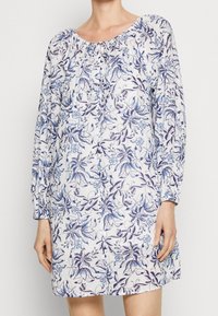 Robe à imprimé floral avec des manches longues, un col élastique et des détails en bouton. Le tissu présente des fleurs bleues et violettes sur un fond clair.