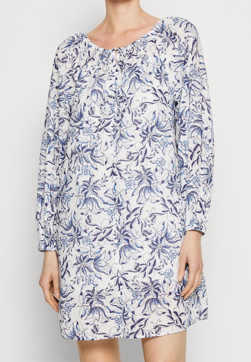Robe à imprimé floral avec des manches longues, un col élastique et des détails en bouton. Le tissu présente des fleurs bleues et violettes sur un fond clair.