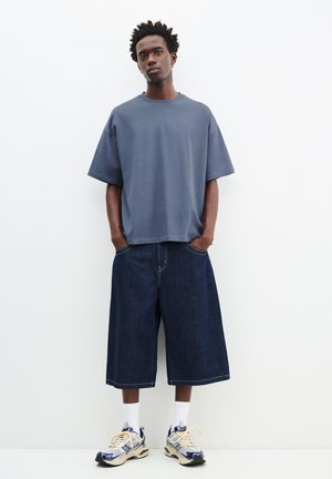 T-shirt en coton gris oversize à manches courtes, associé à des culottes en denim bleu foncé. Porté avec des chaussettes blanches et des baskets multicolores.
