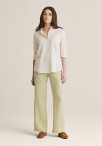 Lettet tekstureret, off-white skjorte med knapper og opkrøllede ærmer samt en brystlomme; parret med løse, lysegrønne linnedbukser og brune slip-on sko.