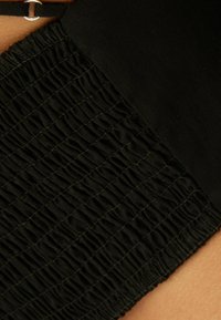 Svart tyg med en texturerad, samlad sektion. De släta sektionerna kontrasterar med den samlade detaljen, vilket skapar en dynamisk visuell effekt.