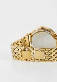 Gold-tone metal bracelet watch with a textured link design and a round case. Features a polished clasp and a glass cover. Clean back design.