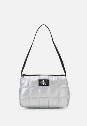 Sac à main argenté matelassé avec une bandoulière noire et un patch logo. Dispose d'une fermeture éclair et d'une forme rectangulaire, fabriqué à partir d'un matériau brillant et rembourré.