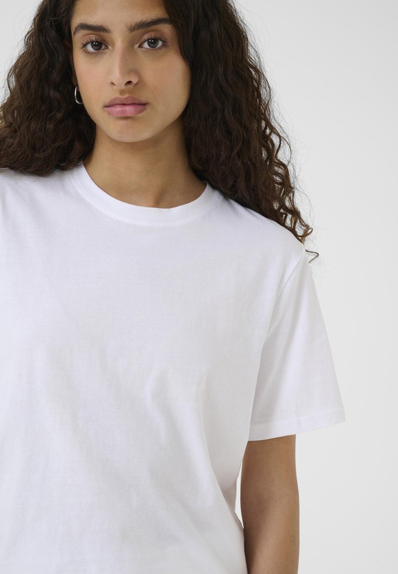 T-shirt bianco in cotone con maniche corte e scollatura rotonda, caratterizzato da una texture liscia e dettagli di cucitura minimi.
