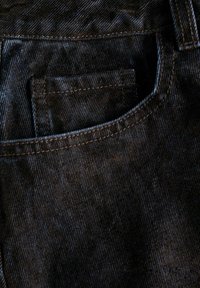 Svart denimtyg med synligt vävningsmönster, med en bakficka och kontrasterande sömmar längs kanterna.