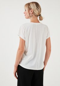 Hvid kortærmet t-shirt lavet af letvægtsstof. Har en afrundet nederste kant og en diskret midtersøm på ryggen.