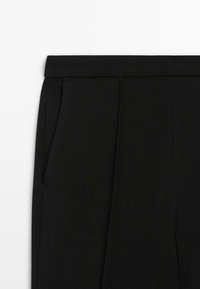 Pantaloni neri su misura con fascia in vita e dettagli sulle tasche laterali su uno sfondo bianco, mostrando la parte anteriore superiore.