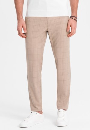 Beige checked trousers with a tailored fit, made from a smooth fabric. Worn with white sneakers, featuring a standard waistband design.